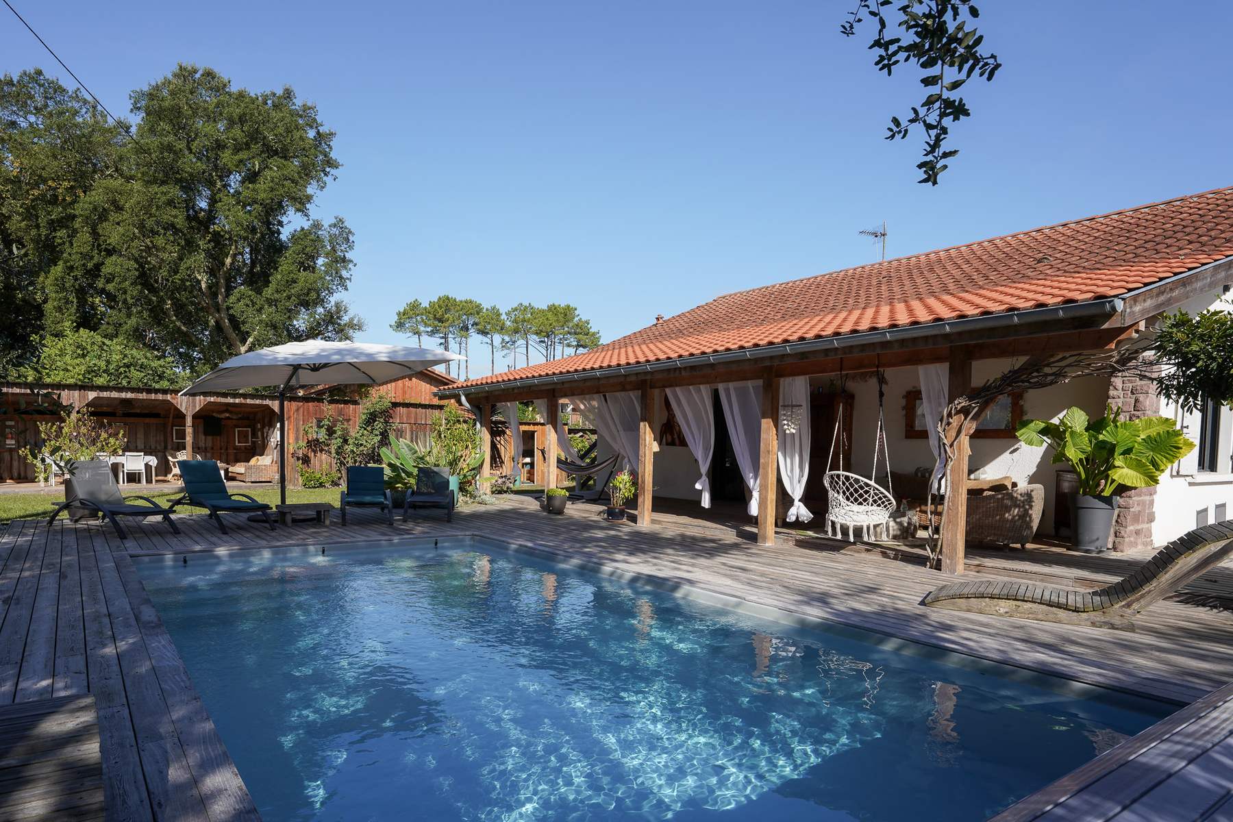 Piscine chauffée de la Villa Naïtika à Seignosse, devant la maison et sa pergola aux voilages blancs